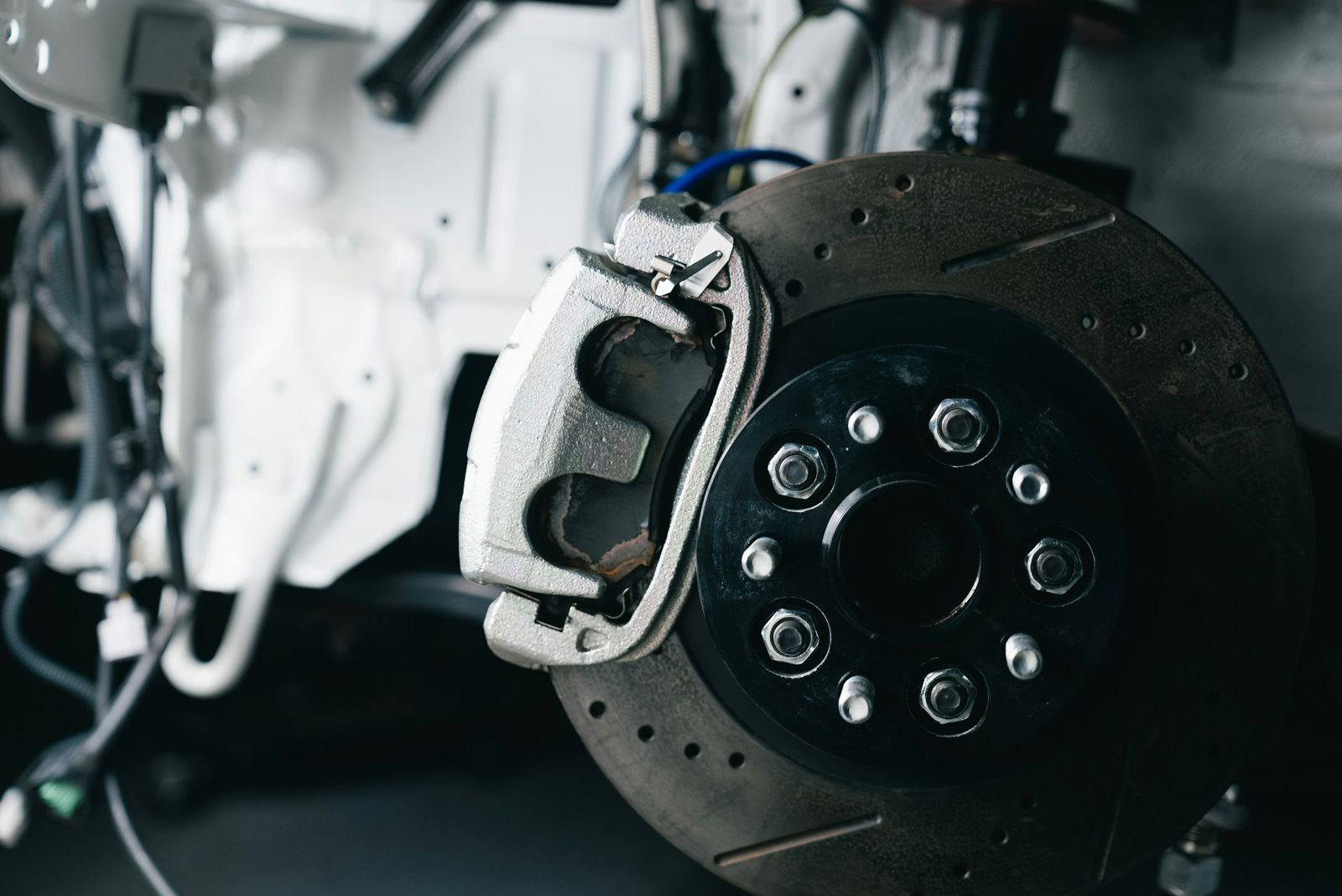 A brake caliper and a drilled disc on a car up on a lift, wheel removed