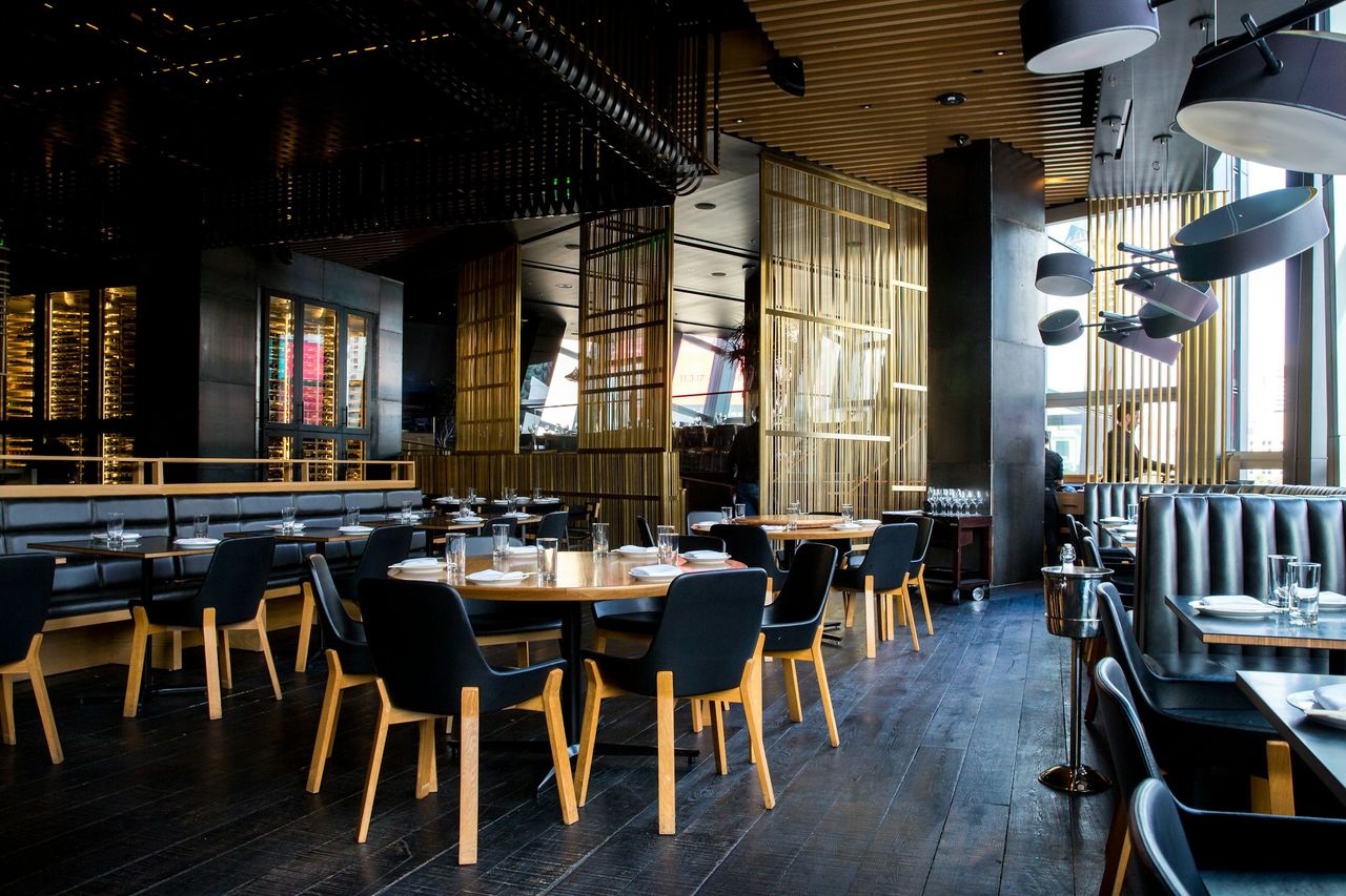 An evening restaurant room with dark chairs, round tables and warm wood panels