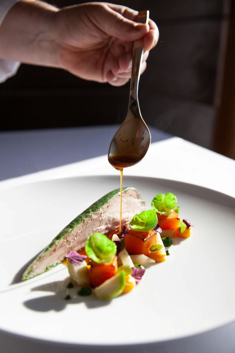 A plated main course with sauce being spooned over it