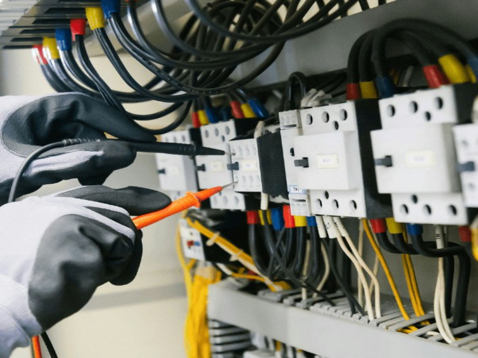 Gloved hands testing the wiring of an electrical panel with meter probes