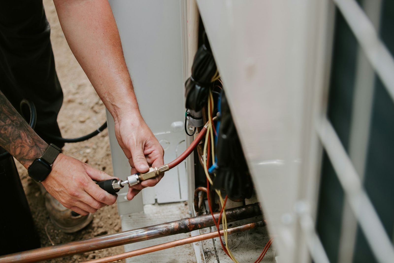 A technician connecting a gauge hose to an outdoor heat pump unit