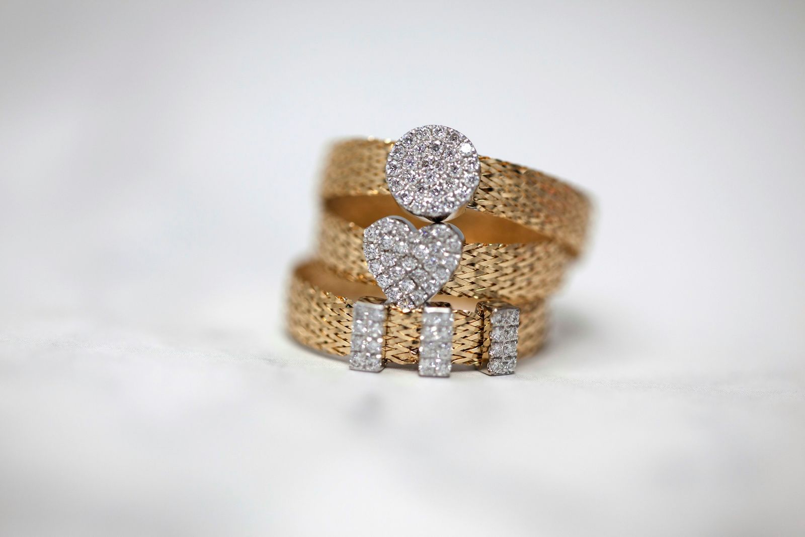 Three stacked gold mesh rings set with small white stones, on a pale background