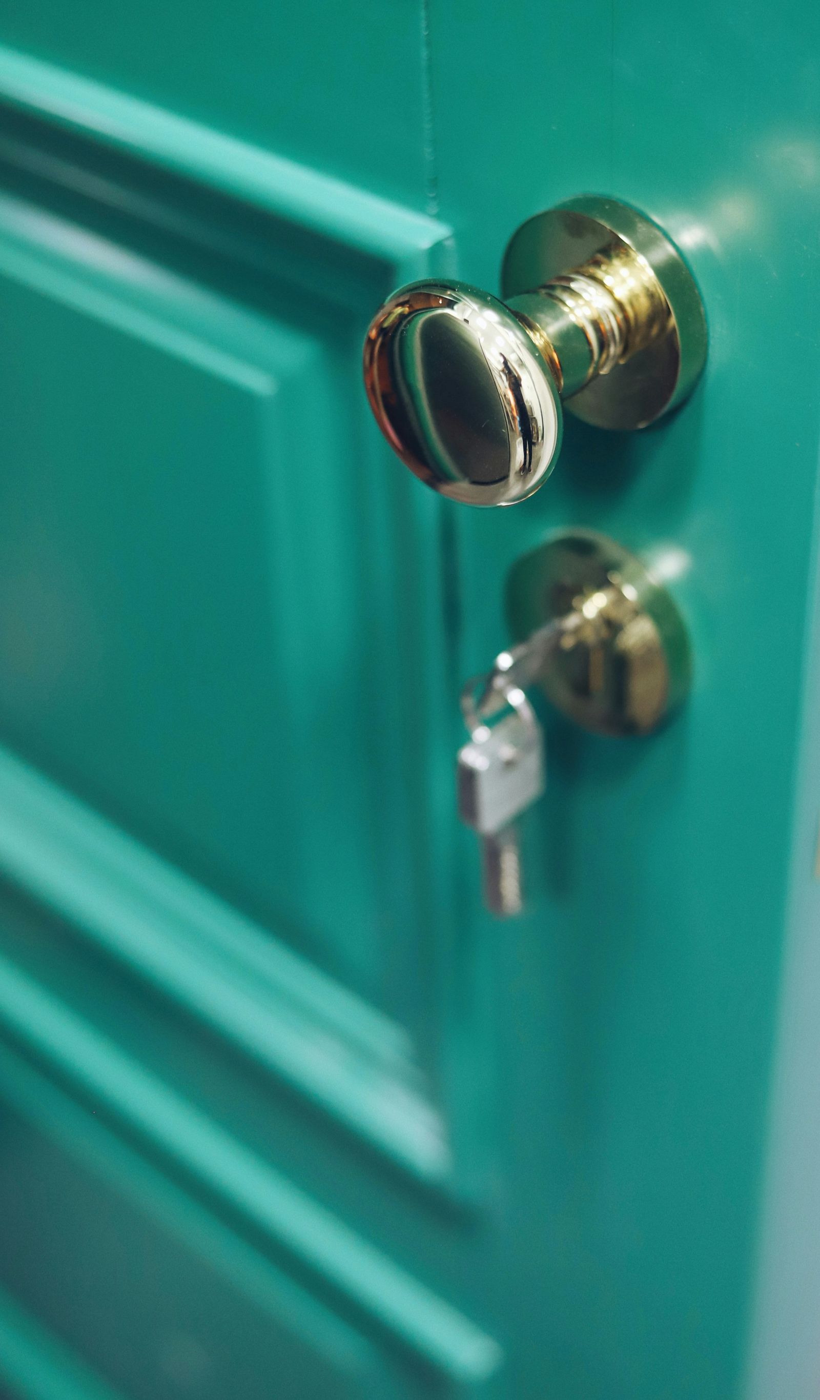 A brass knob and a deadbolt with a key in it, on a teal front door