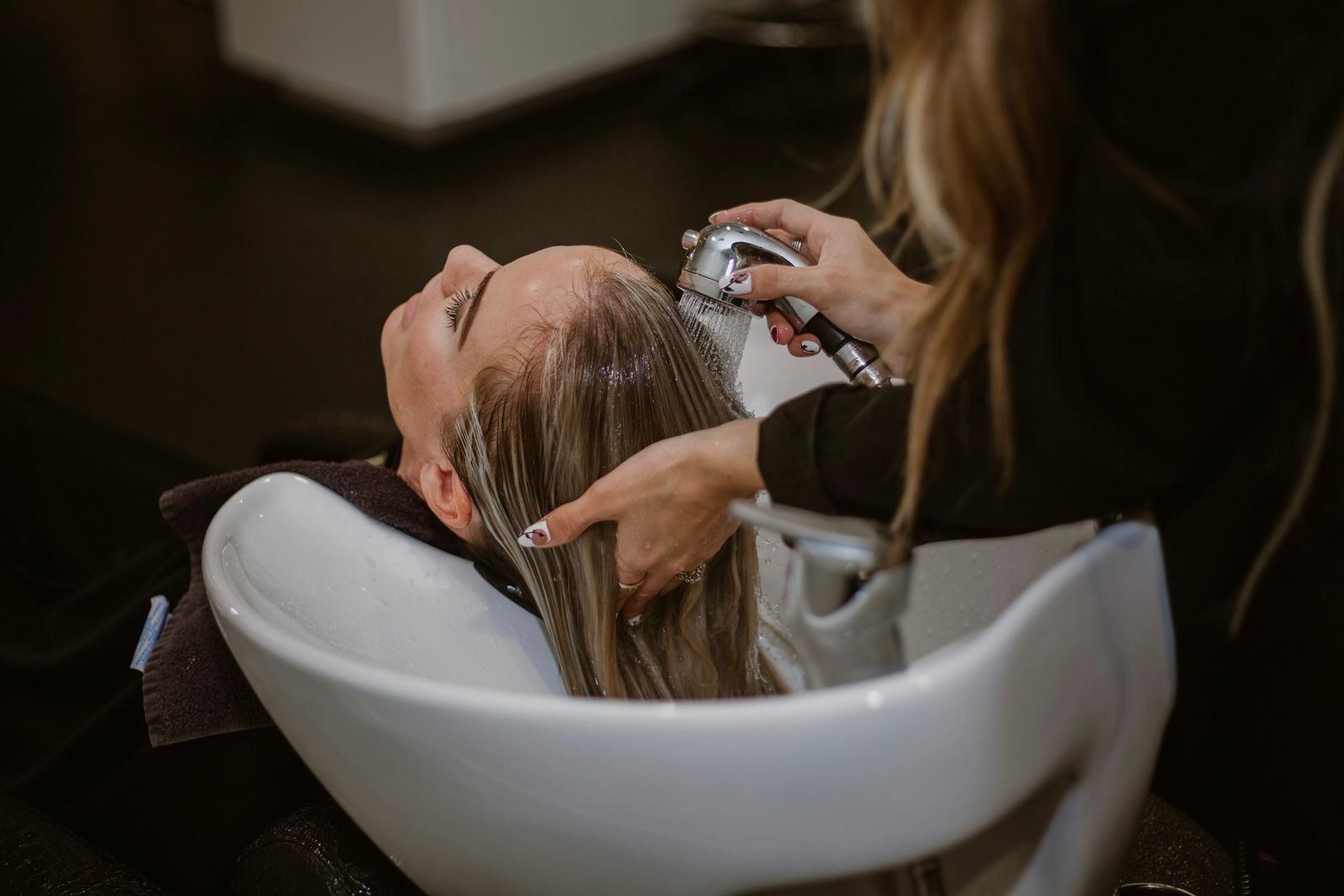 A stylist washing a client’s hair at a salon basin