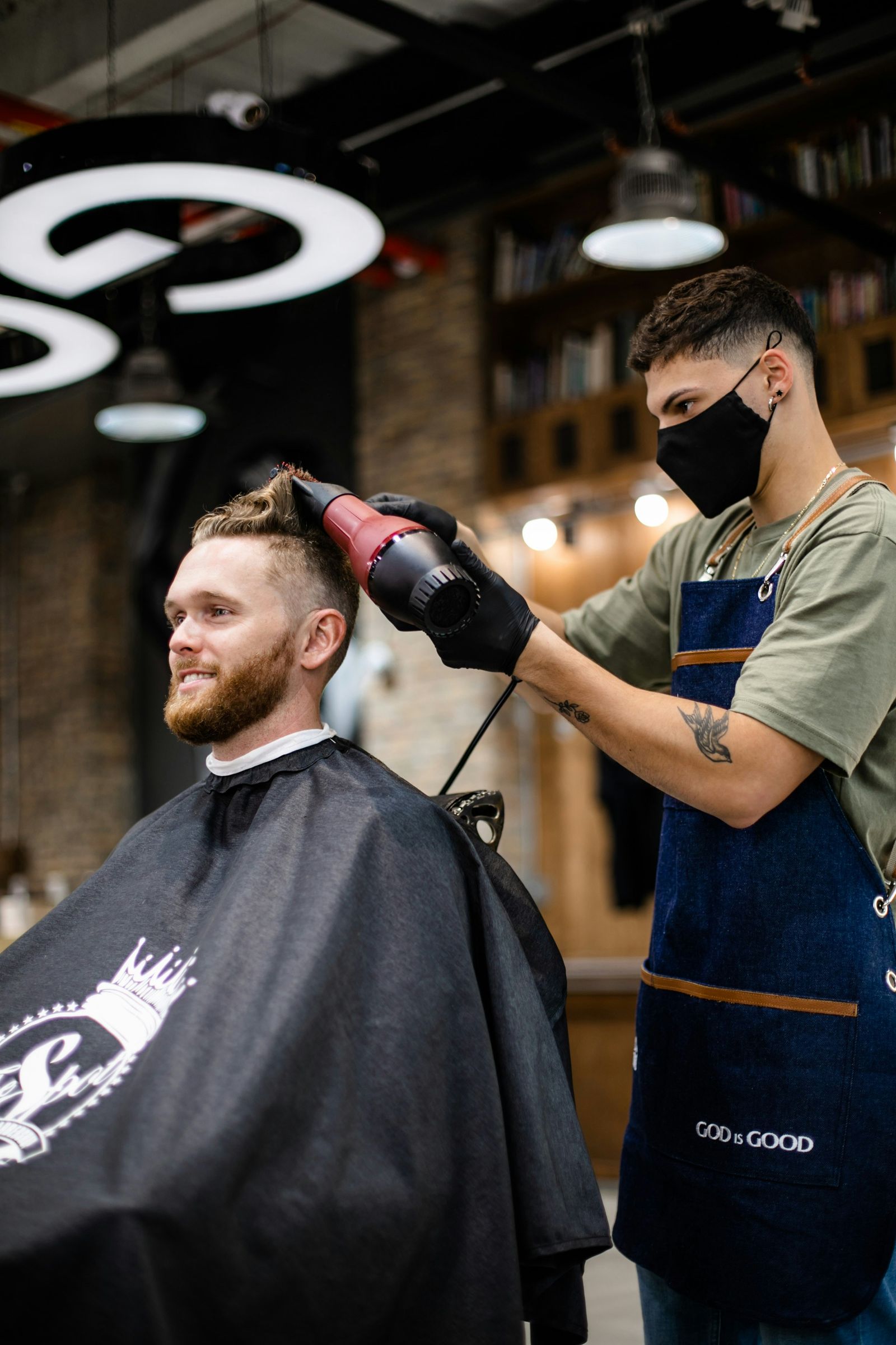 A barber blow-drying a smiling client’s hair in a studio