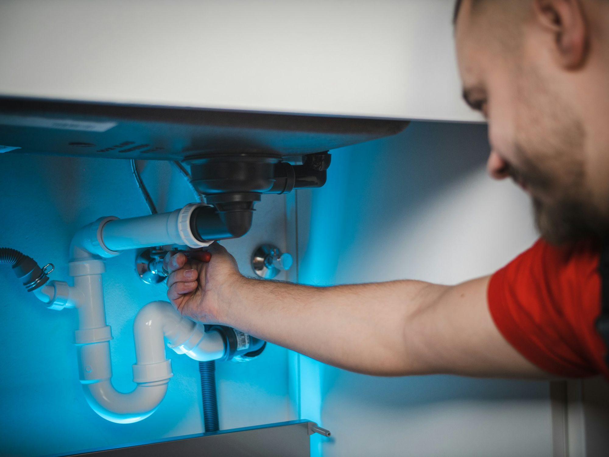 A plumber tightening the drain pipe under a sink